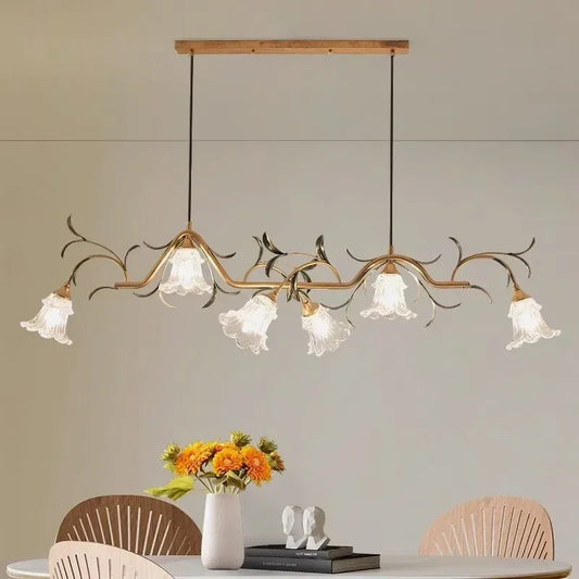 A gold floral branch-style pendant light with six frosted glass shades hanging above a dining table.