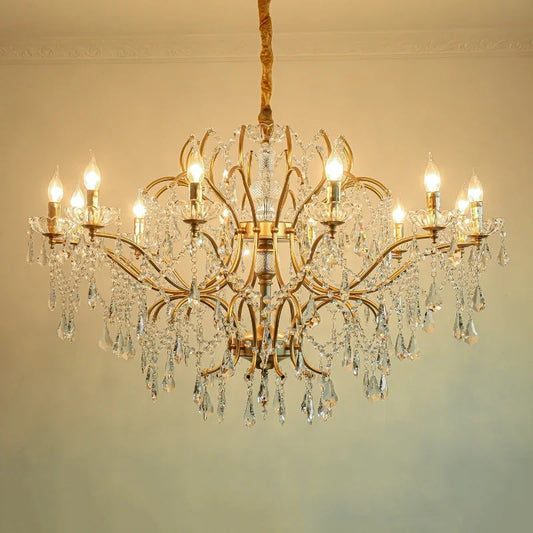 Close-up of a gold chandelier showcasing intricate crystal droplets and polished metal arms, lit by warm bulbs.