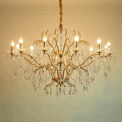 Close-up of a gold chandelier showcasing intricate crystal droplets and polished metal arms, lit by warm bulbs.