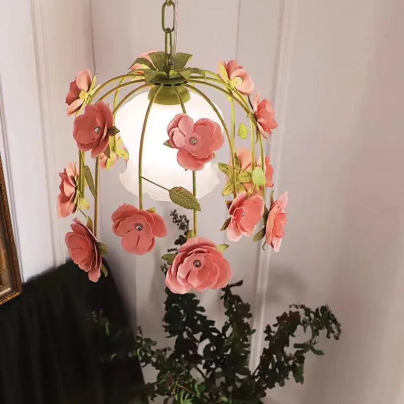 A decorative gold chandelier with pink floral accents hanging in a room, featuring a glass diffuser.