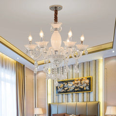 A black and crystal candelabra chandelier with five illuminated bulbs, installed in a bedroom setting with a headboard and curtains.