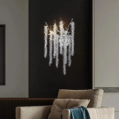 A single gold crystal branch wall sconce mounted on a dark wall above a chair, showcasing its intricate design.