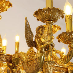 Close-up of the gold chandelier showing a detailed mermaid figure with wings holding a central stem.