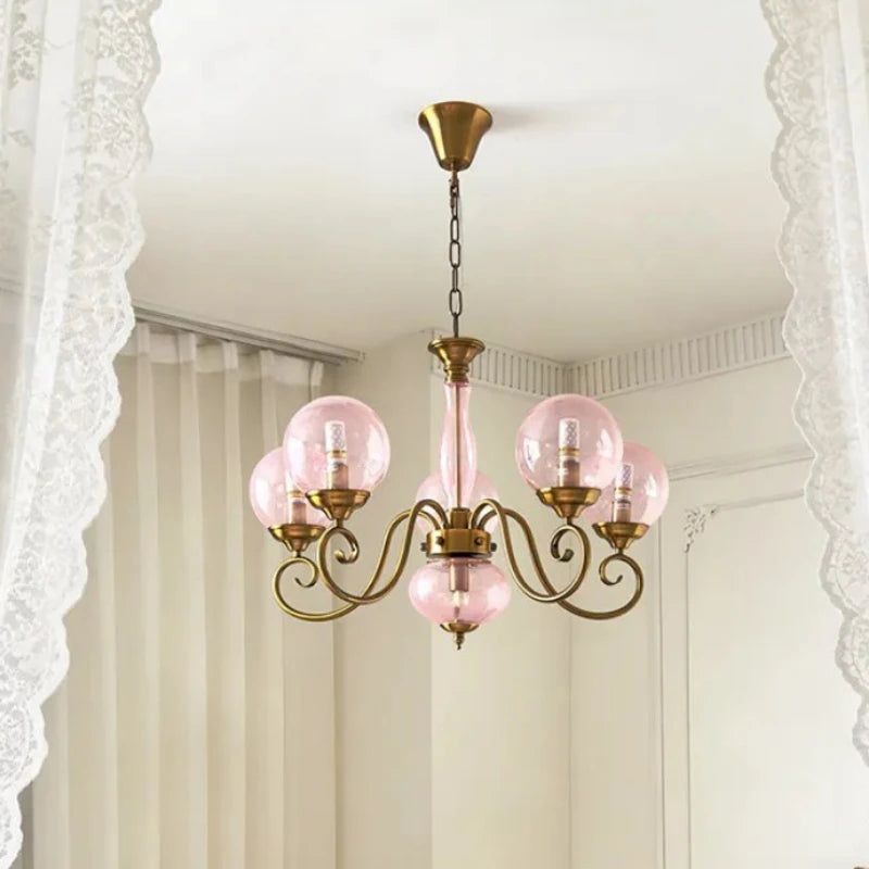 A gold-finished pendant light with pink glass globes hanging from the ceiling, framed by white lace curtains.