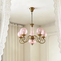A gold-finished pendant light with pink glass globes hanging from the ceiling, framed by white lace curtains.