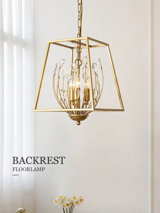 A gold metal cage pendant light with clear teardrop-shaped crystals hanging, shown in a softly lit room with a sheer curtain in the background.