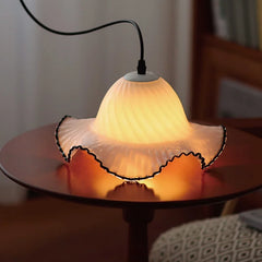 White glass fluted pendant light with black trim resting on a wooden table, casting a warm glow.
