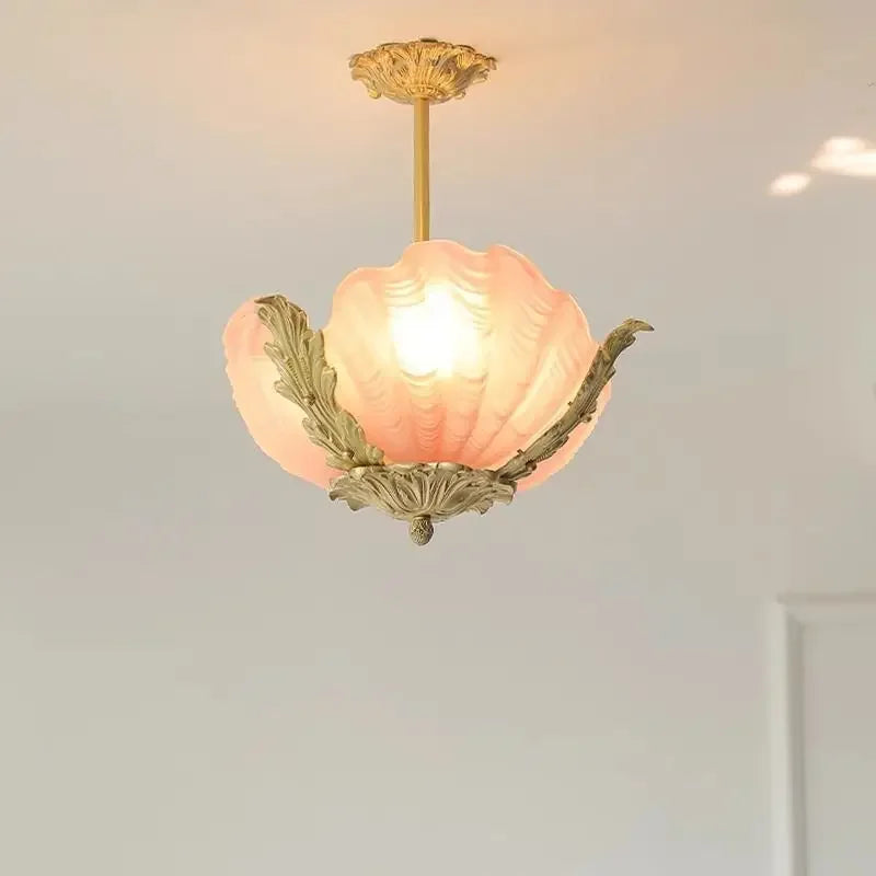 Close-up of a pink shell-shaped glass pendant light with ornate gold leaf accents, illuminated from within.