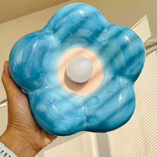 Hand holding a blue ceramic petal wall sconce with a soft white bulb in the center.