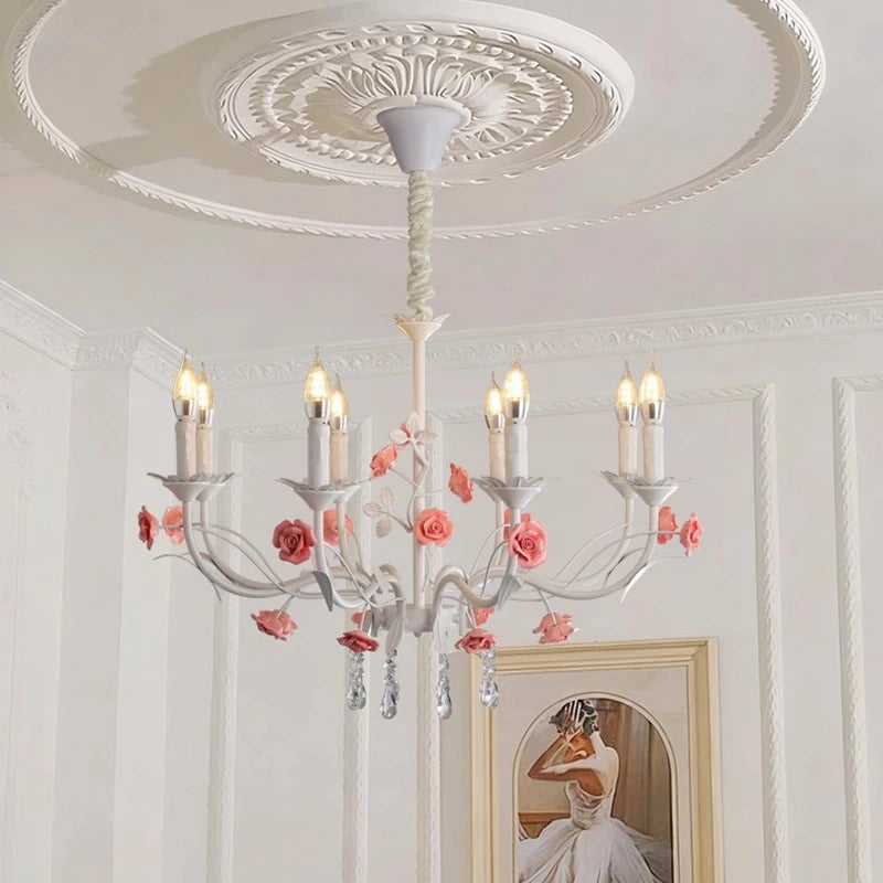 Close-up of a white floral crystal candelabra chandelier with pink roses, installed on a white ceiling.
