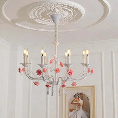 Close-up of a white floral crystal candelabra chandelier with pink roses, installed on a white ceiling.