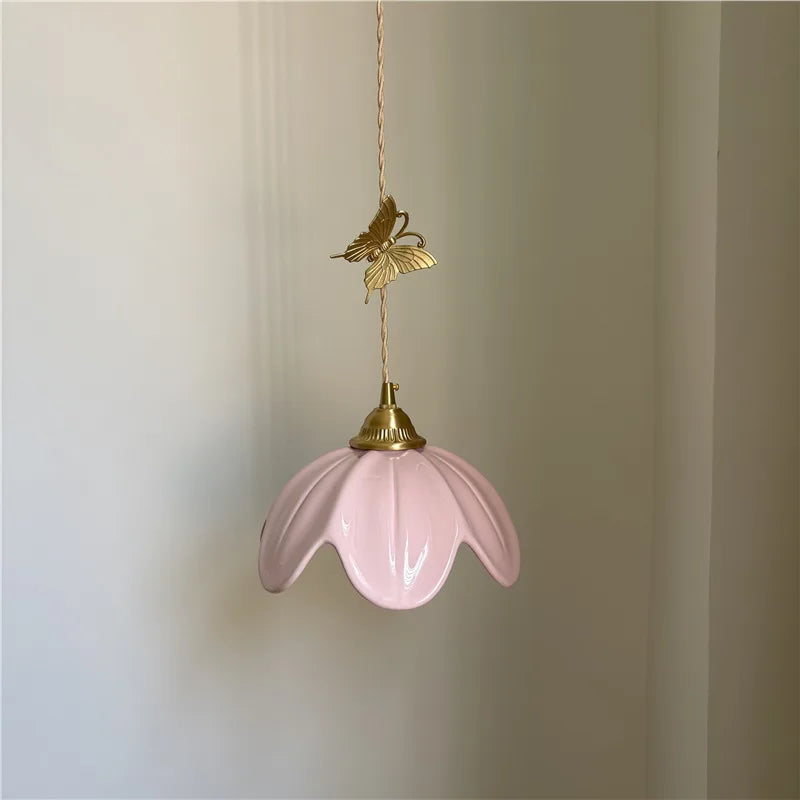 Pink ceramic petal pendant light with a brass butterfly accent hanging against a white wall.