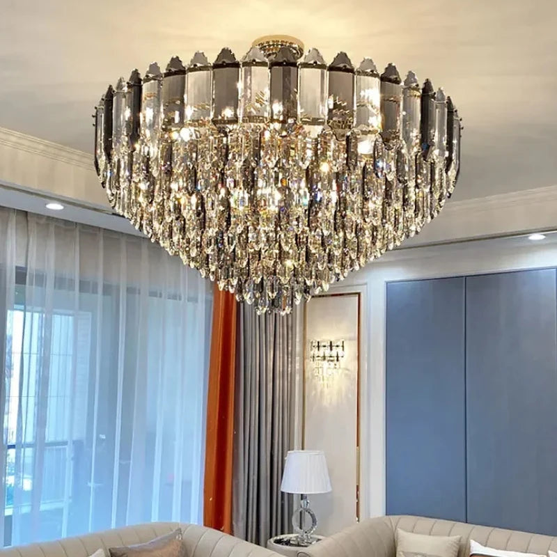 A large, multi-tiered chandelier with a gold-toned metal frame and numerous clear, faceted crystal droplets cascading downwards, suspended from a ceiling in a well-lit room.