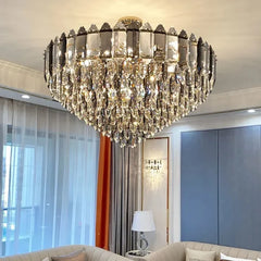 A large, multi-tiered chandelier with a gold-toned metal frame and numerous clear, faceted crystal droplets cascading downwards, suspended from a ceiling in a well-lit room.