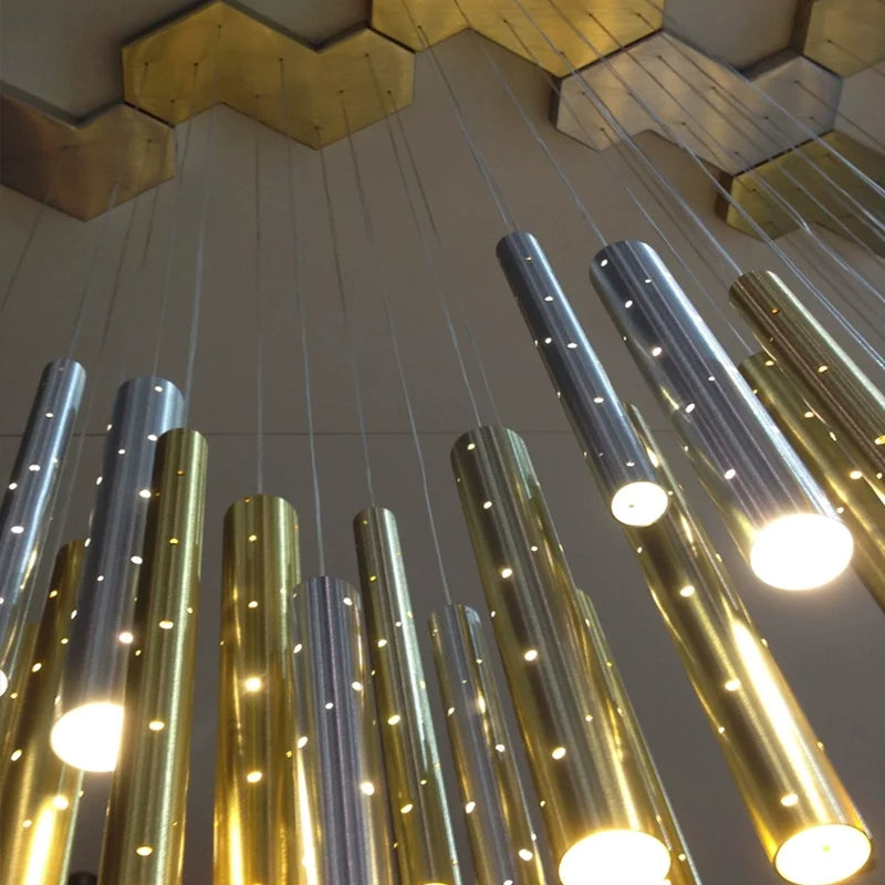 Extreme close-up of the illuminated cylindrical tubes of a modern chandelier, showing the brushed gold and silver finishes and the small integrated lights.