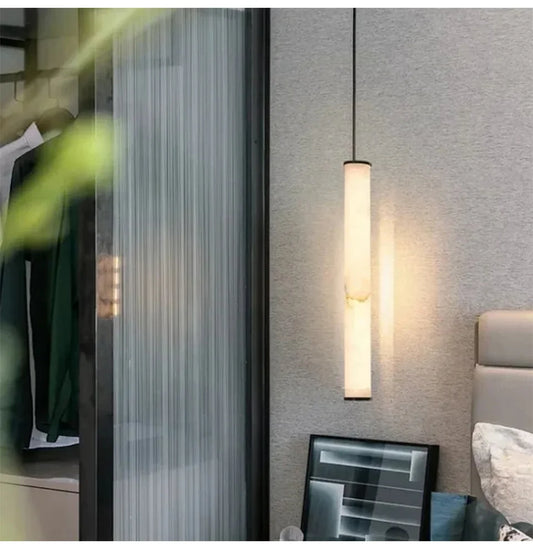 Close-up of a marble cylinder pendant light with natural stone textures, casting a warm glow against a textured wall.