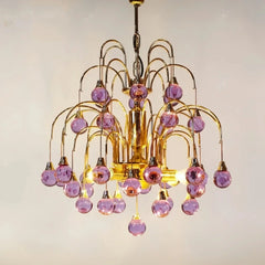 Gold chandelier with cascading purple teardrop glass pendants against a white background