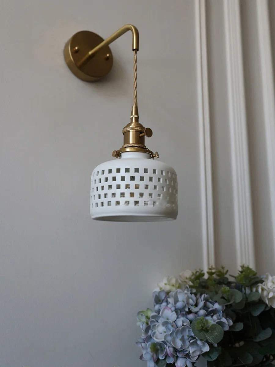 Wall-mounted light fixture with white ceramic shade and gold arm on a neutral wall.