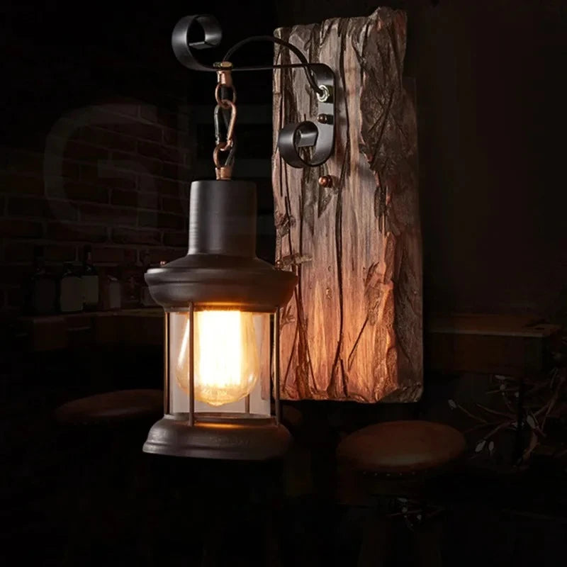 A black iron lantern wall sconce with a distressed wood backplate, casting a warm glow in a dimly lit room with brick accents.