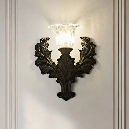 Black resin wall sconce with ornate detailing and a fluted glass shade, mounted on a white wall.