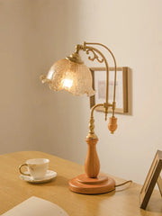 Side view of a wooden base table lamp with a textured glass shade and brass arm, showcasing its design elements against a wall.