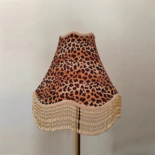 A leopard print fabric bell lampshade with beaded fringe shown against a plain wall.