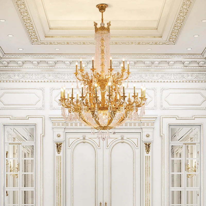 A gold tiered crystal candelabra chandelier in an ornate white room with detailed wall moldings and mirrored doors.