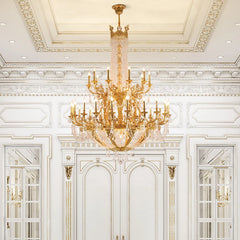 A gold tiered crystal candelabra chandelier in an ornate white room with detailed wall moldings and mirrored doors.