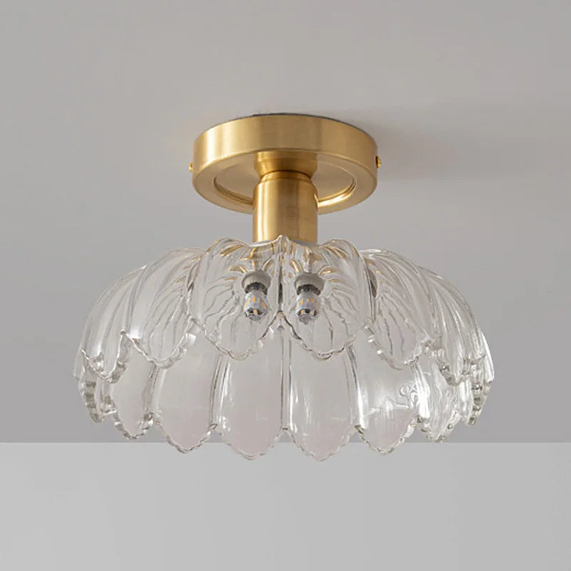 A flush mount ceiling light with a gold metal base and a decorative clear glass shade that resembles layered petals.
