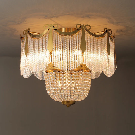 A gold and crystal tiered chandelier mounted on a ceiling, illuminated with warm light.