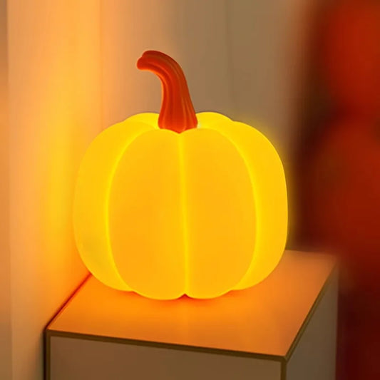Side view of a glowing orange pumpkin table lamp with a red stem placed on a small wooden surface.