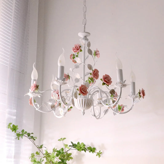 Close-up of a white iron chandelier with pink roses and green leaves, hanging indoors.