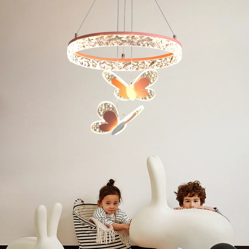 A pink crystal ring pendant light with three butterfly accents hanging over two children in a room.