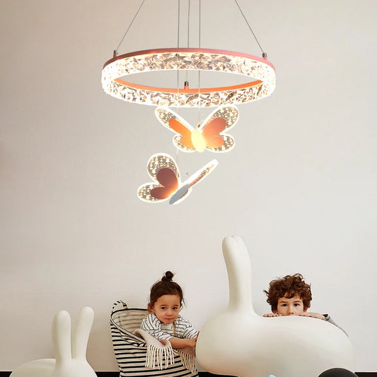 A pink crystal ring pendant light with three butterfly accents hanging over two children in a room.