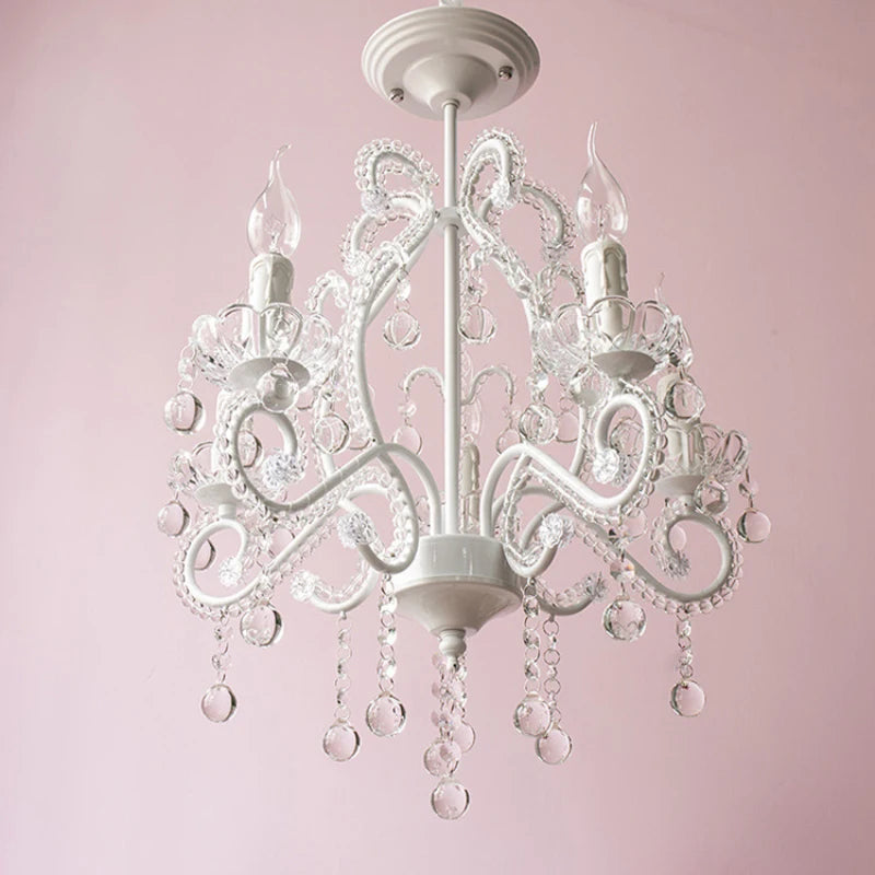 A white candelabra chandelier featuring crystal droplets hanging from its arms, illuminated against a pink wall.