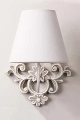 Front view of a gray-white wood wall sconce with a fabric shade and detailed floral scrollwork on a white wall.