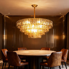 A multi-tiered gold chandelier with amber glass accents hanging over a round marble dining table with brown leather chairs.