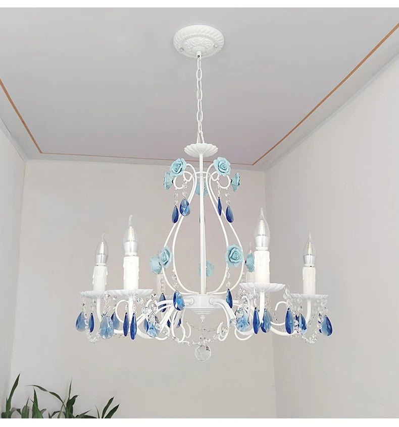 Low-angle view of a white semi-flush mount chandelier with blue floral details and crystal prisms, mounted on a white ceiling.