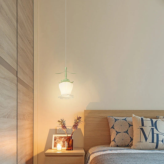A flower-shaped pendant light hanging above a nightstand next to a bed in a bedroom, casting a warm glow.