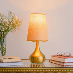 A gold table lamp with a crystal base on a glass table with books and flowers.