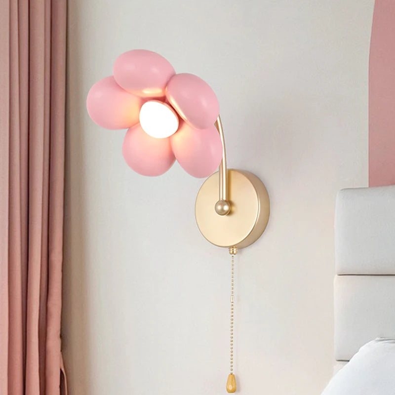Pink floral wall lamp with gold arm on a light gray wall.