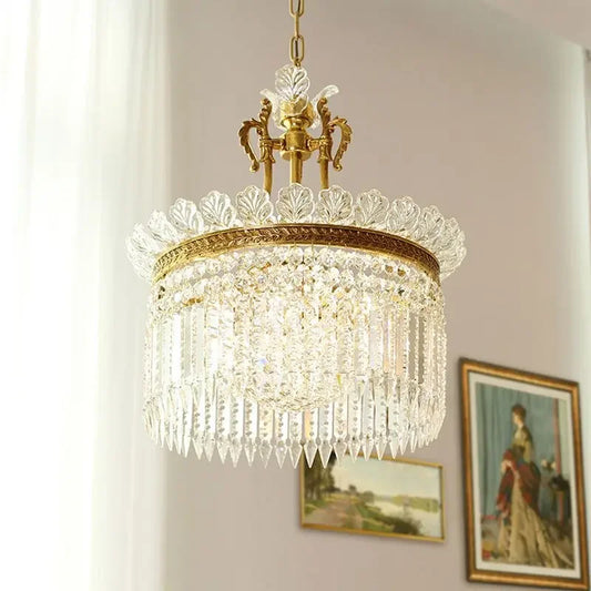 A gold and crystal tiered chandelier with cascading teardrop crystals, shown in a room with framed artwork on the wall.
