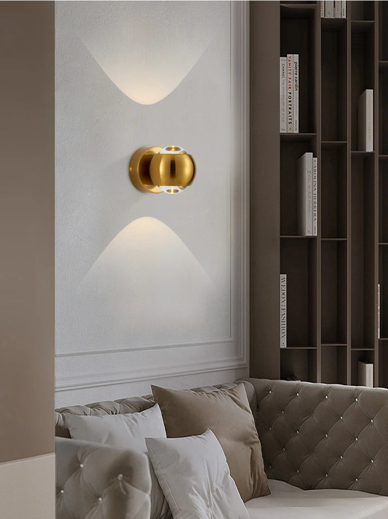Gold wall sconce on a white wall with a bookshelf and sofa in the background