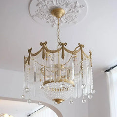 Side view of a gold crystal chandelier featuring cascading glass rods and a central crystal bowl, mounted on a chain.