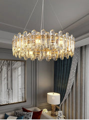 A gold chandelier with crystal accents, showcasing its tiered design against a backdrop of elegant curtains and artwork.