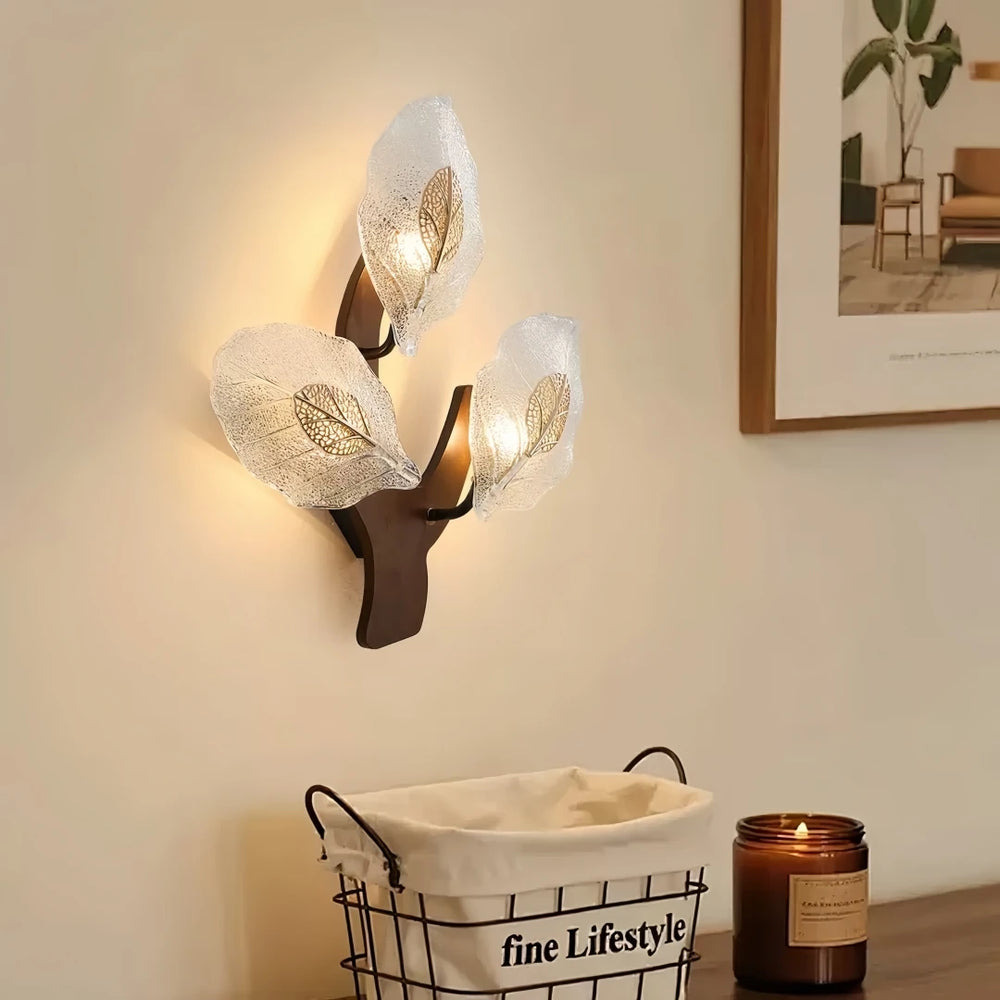 Close-up of a wood leaf wall sconce with two frosted glass shades, mounted on a dark wood base, with a basket and candle below.