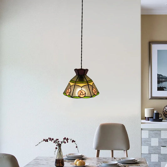 A glass floral pendant light with green and yellow accents hanging above a dining table.
