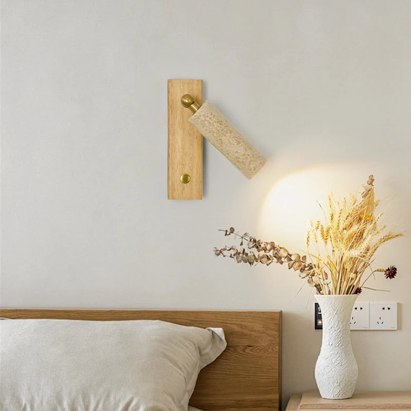 Wooden wall sconce lighting a room with a vase of dried flowers on a nightstand.
