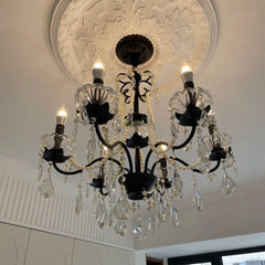 Close-up of a black candelabra chandelier with crystal and pearl details, mounted on a decorative white ceiling medallion.