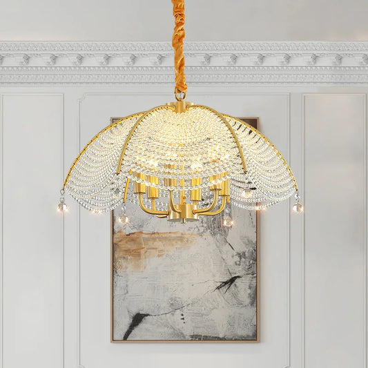 A wide shot of a gold-finish fan-shaped crystal chandelier hanging in a room with a painting on the wall and decorative molding, showcasing its scale.